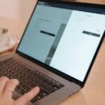 A close-up view of a person using a laptop on a wooden table indoors, creating a warm and professional atmosphere.