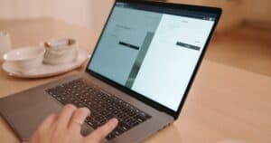 A close-up view of a person using a laptop on a wooden table indoors, creating a warm and professional atmosphere.