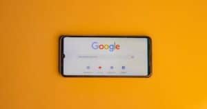 Smartphone displaying Google search page on a vibrant yellow background.