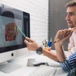 Side view of focused coworkers working together on graphic design while sitting at table and looking at monitor in modern office