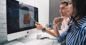 Side view of focused coworkers working together on graphic design while sitting at table and looking at monitor in modern office