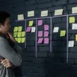Adult male focusing on task planning using sticky notes on a black wall in a contemporary office setting.