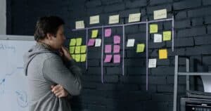 Adult male focusing on task planning using sticky notes on a black wall in a contemporary office setting.
