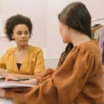 Two women discussing a fashion business strategy indoors with clothing rack.
