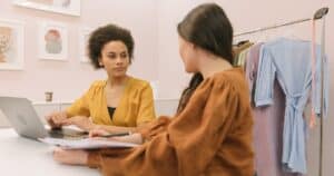 Two women discussing a fashion business strategy indoors with clothing rack.