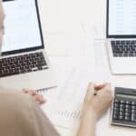 Two people analyzing business data on laptops with charts and graphs.