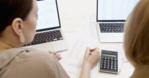 Two people analyzing business data on laptops with charts and graphs.
