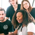A diverse group of young professionals collaborating around a laptop in a modern office setting. Perfect for business or tech concepts.