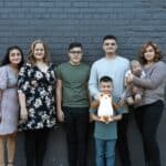 A joyful multigenerational family posing in front of a gray brick wall, symbolizing unity and togetherness.