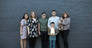 A joyful multigenerational family posing in front of a gray brick wall, symbolizing unity and togetherness.