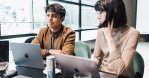 Young professionals collaborate on laptops in a bright, modern office space.