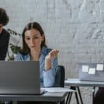 Three professionals working together in a contemporary office space, focused on a laptop task.