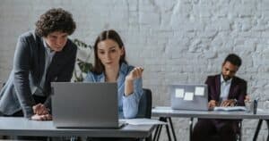 Three professionals working together in a contemporary office space, focused on a laptop task.